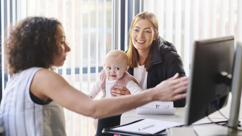 woman showing other woman with baby something on the computer monitor