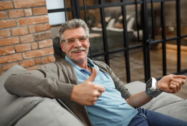 old man smiling giving thumbs up with right hand with blood pressure meter on left wrist