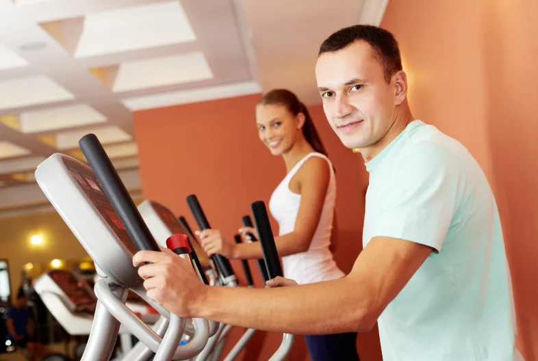 man and women in gym on elliptical machine smiling