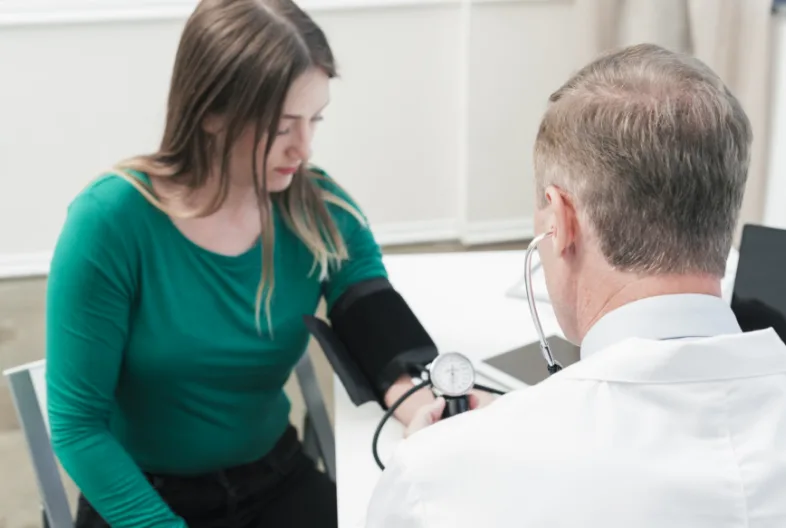 women in green long sleeve shirt in drs office getting blood pressure taken by the dr