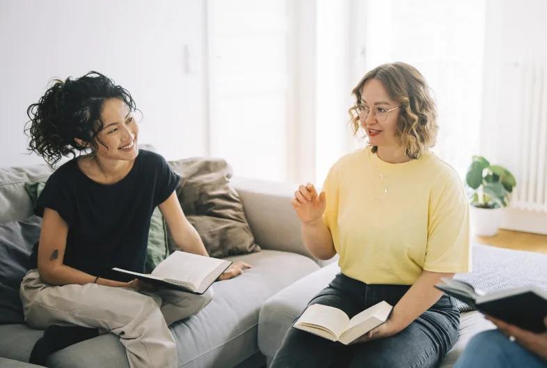 2 women speaking while holding books