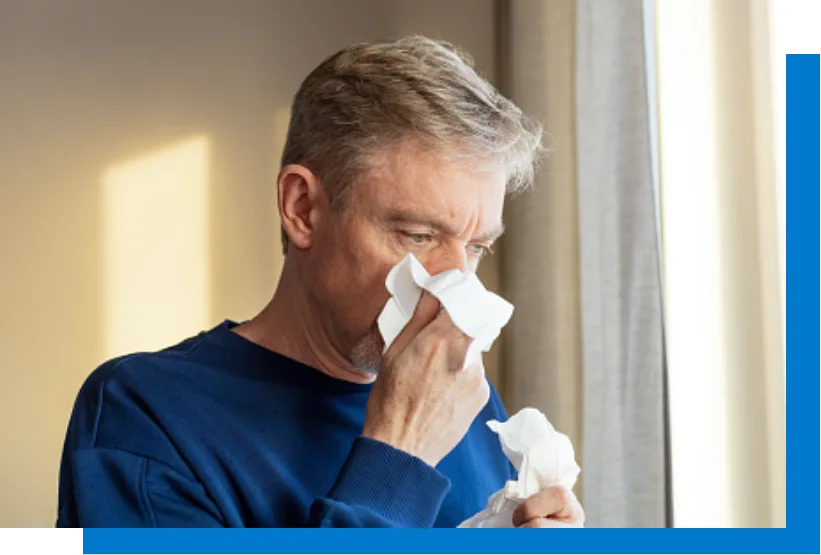 A man in a blue sweater is blowing his nose into a tissue.