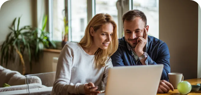 Couple smiling while reviewing contents on a laptop at a breakfast table