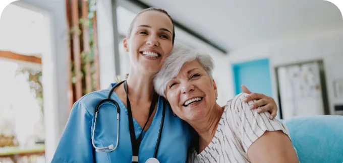 Nurse in blue scrubs holding older lady both smiling