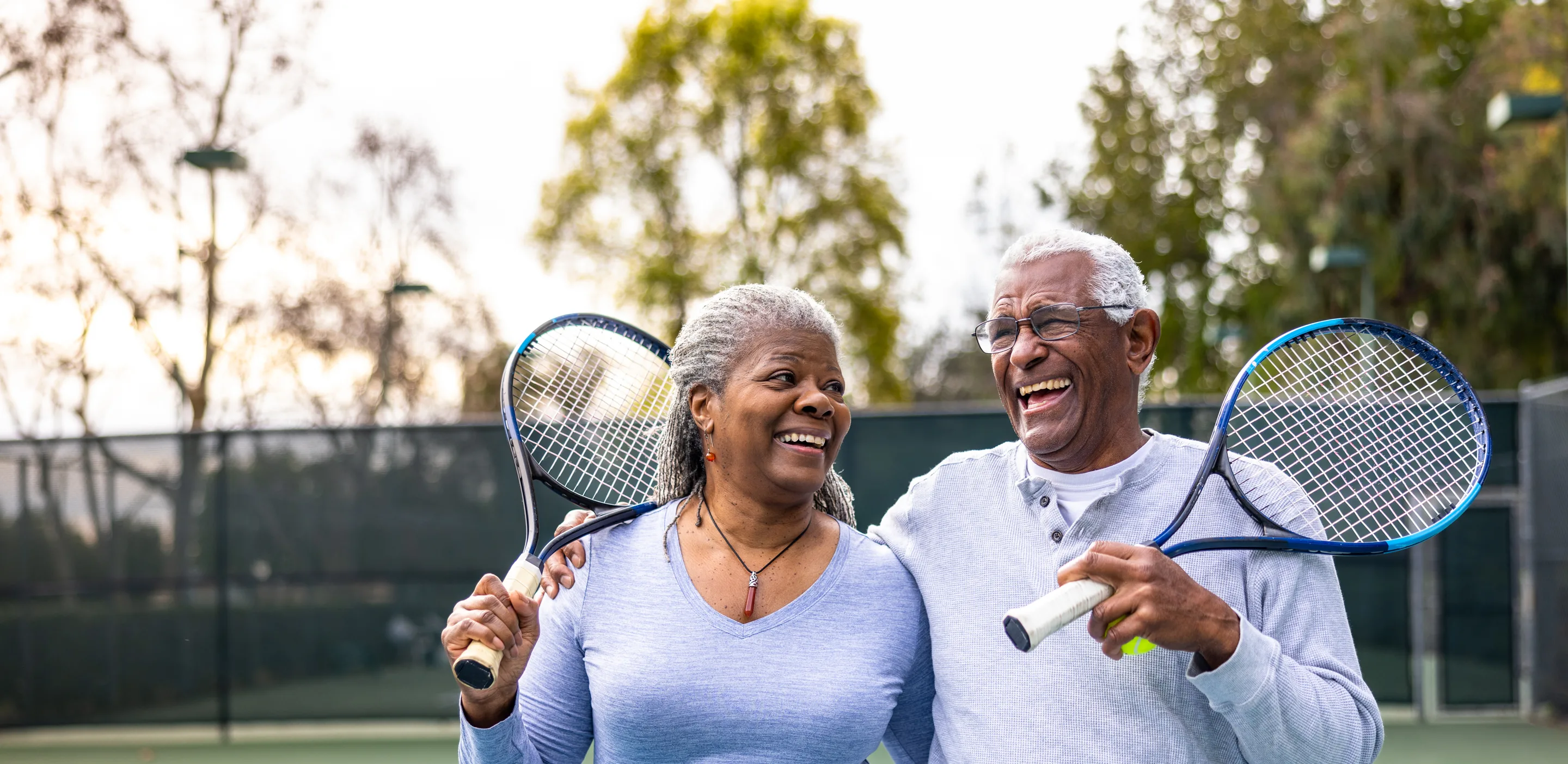 Couple outside on a tennis court smiling while holding their tennis racquet