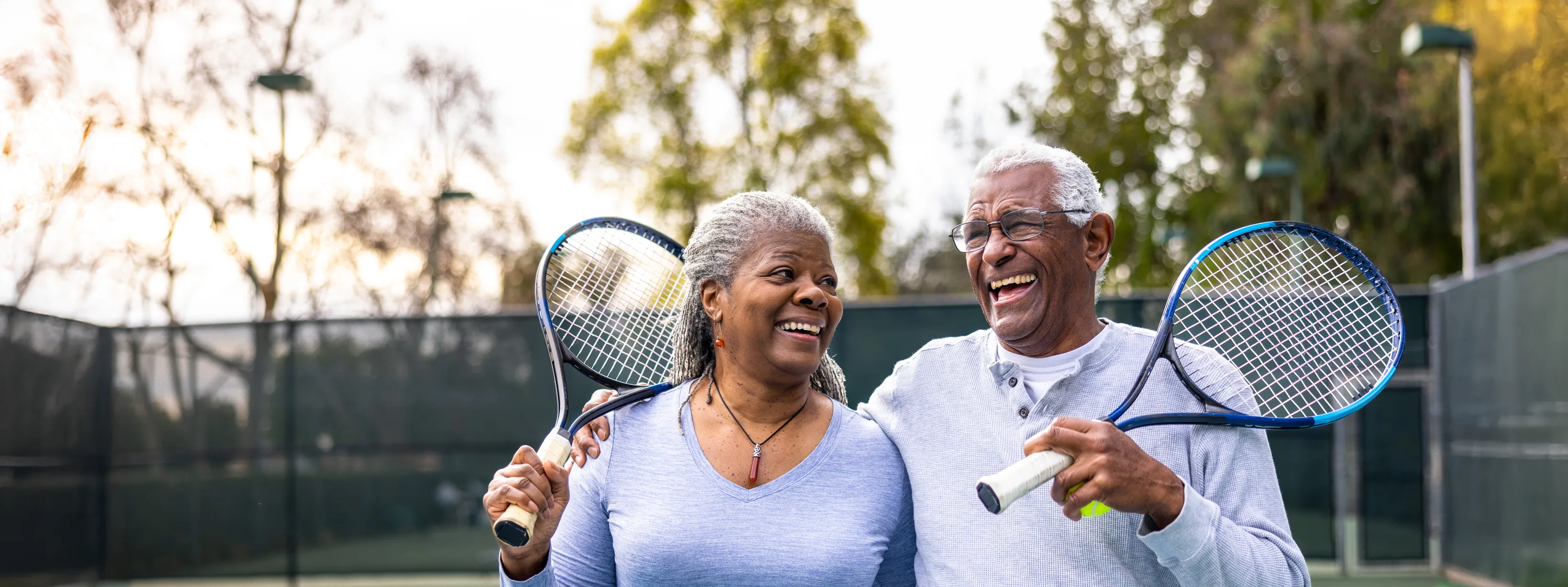 Couple outside on a tennis court smiling while holding their tennis racquet