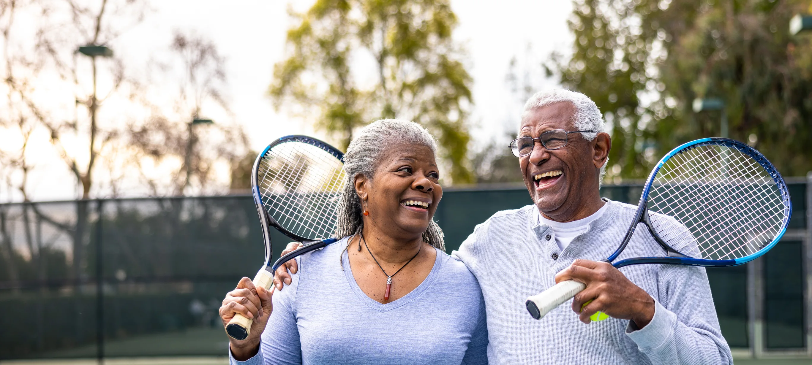 Couple outside on a tennis court smiling while holding their tennis racquet