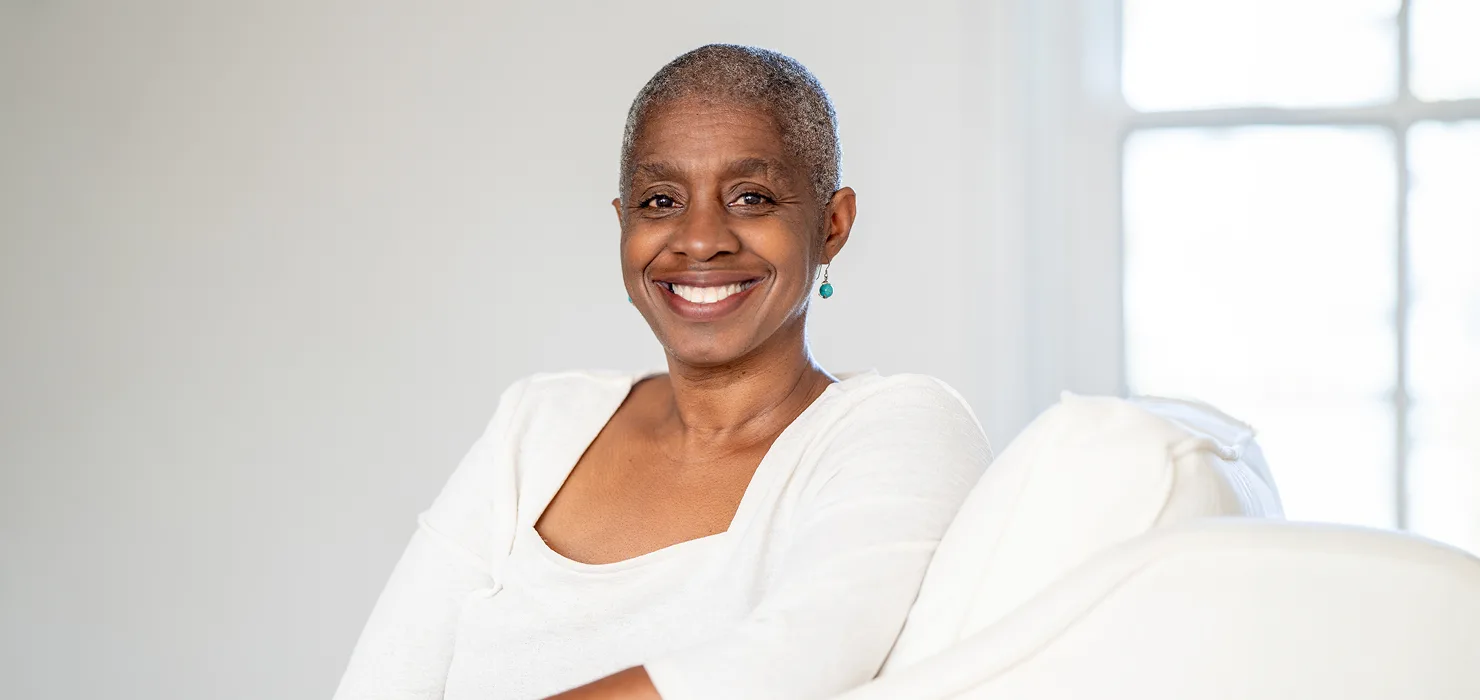 woman in her 50's sitting & smiling on a couch