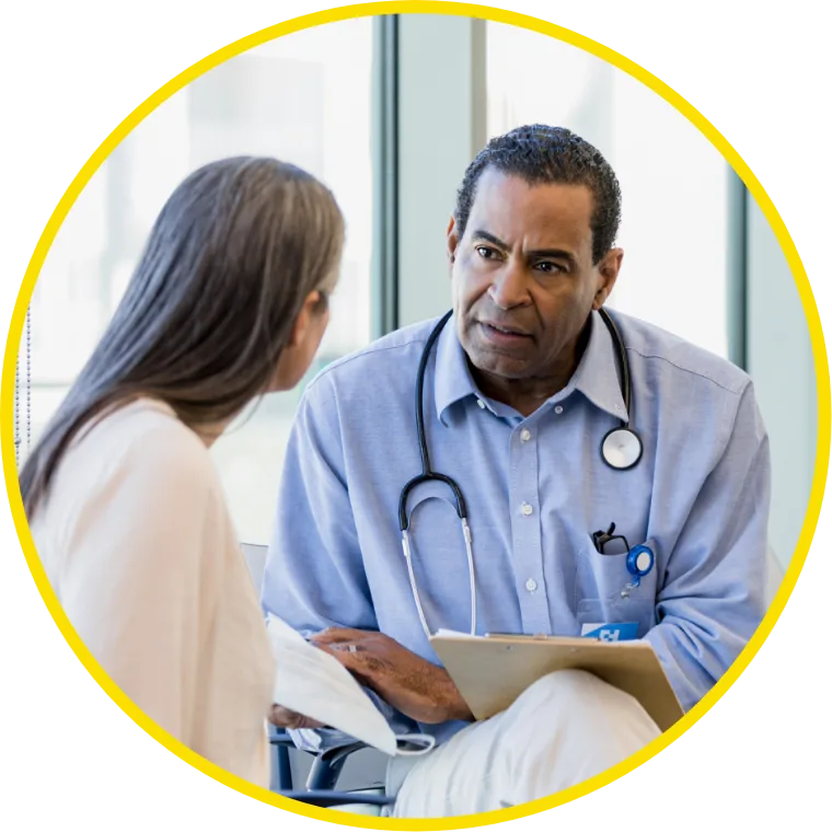 A doctor attentively listens to a patient in an office setting, showing empathy. The doctor wears a stethoscope and holds a clipboard.