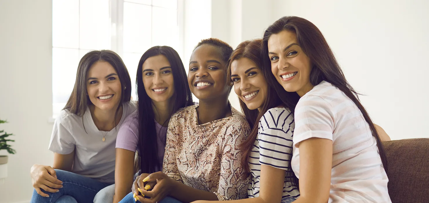 four women in their thirties smiling & sitting together