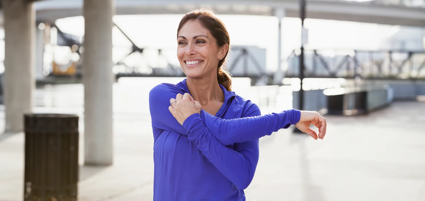 smiling, middle-aged woman stretches prior to walking or jogging outside