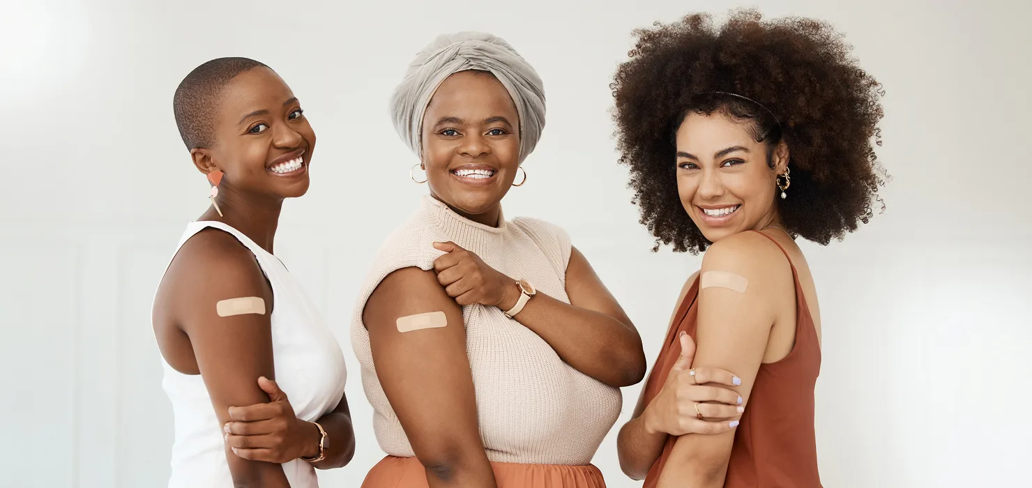 three women in their twenties smiling & laughing together as they get vaccinated