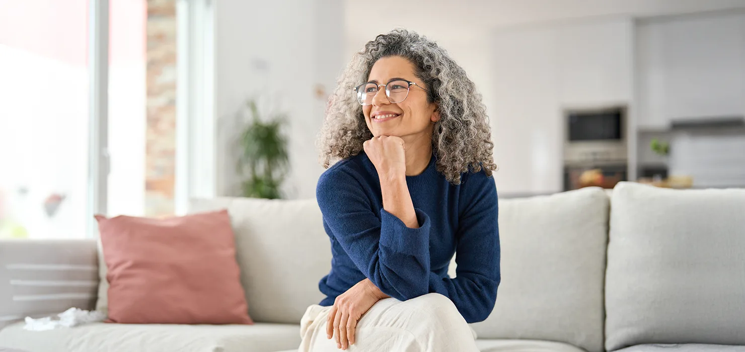 woman in her 50's sitting & smiling on a couch
