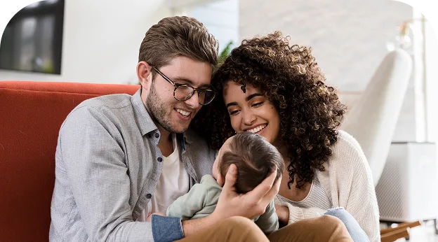 image of a young couple sitting on a couch & holding a newborn