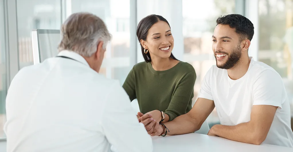 a man, pregnant woman, & young girl talking with a doctor in the office