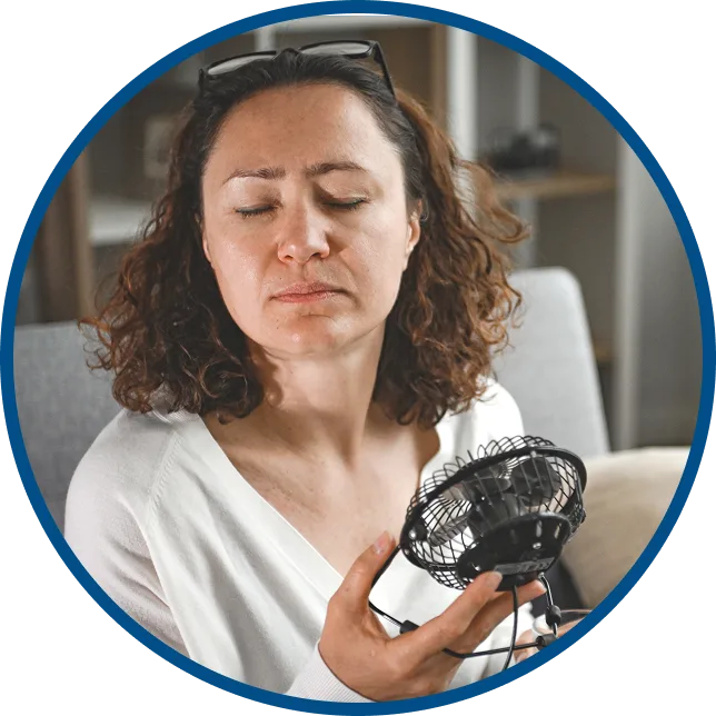 woman experiencing a hot flash & pointing a fan at herself