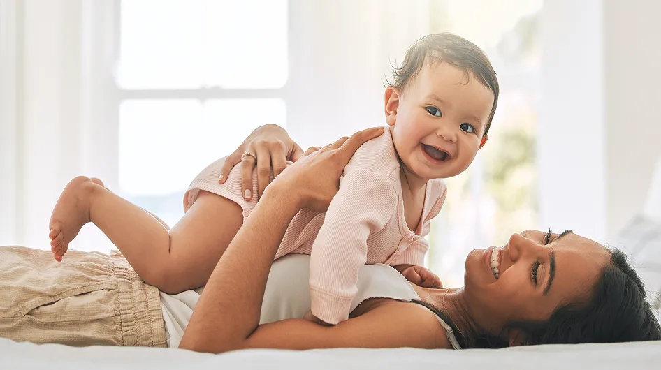 a woman lying on her back & smiling while looking at the baby that she's holding
