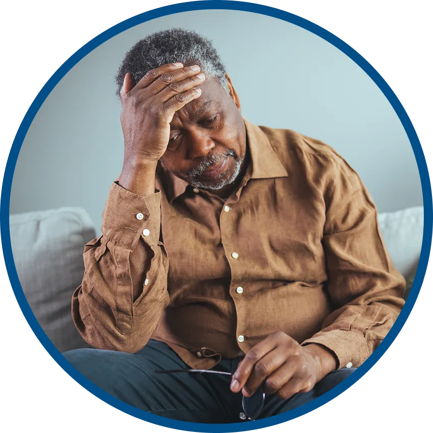 Older man sitting with hand on forehead, looking unwell and holding his glasses