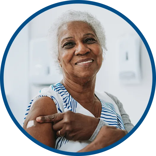 Smiling older woman pointing to her arm with a bandage after receiving a vaccination